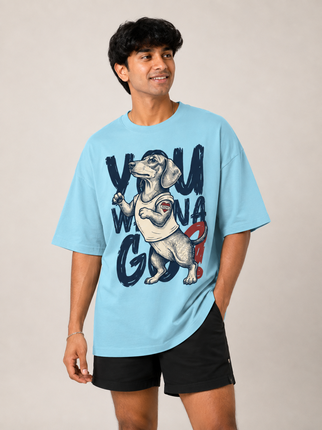 A man wearing a light blue graphic t-shirt with a dachshund and the text 'YOU WILL WIN' on the front, paired with black athletic shorts, against a plain beige background.